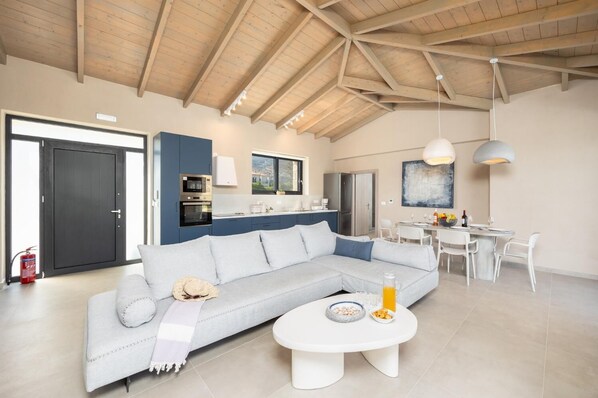 A modern living room with a light grey sofa, a white coffee table, and a dining area with a white table and chairs.