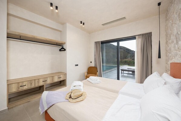 Una camera d'albergo con un letto grande, una panca in legno, una sedia e vista su una piscina e montagne.