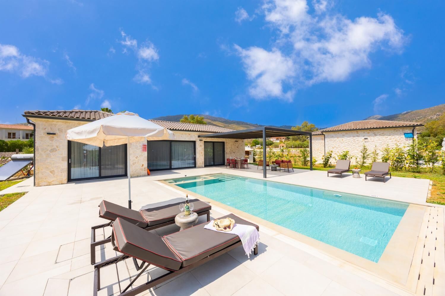 A modern villa with a swimming pool, outdoor seating, and a stone facade.