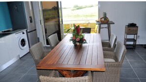 A dining area with a wooden table and wicker chairs, a washing machine, and a view of the outdoors.