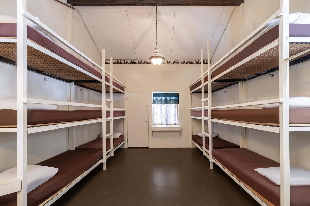 Un dormitorio con literas dispuestas en dos filas, una ventana con cortinas y una lámpara colgante.