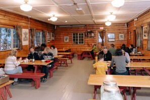 Ein Essbereich im Holzblockhaus-Stil mit Tischen, Bänken, großen Fenstern und Deckenventilatoren.