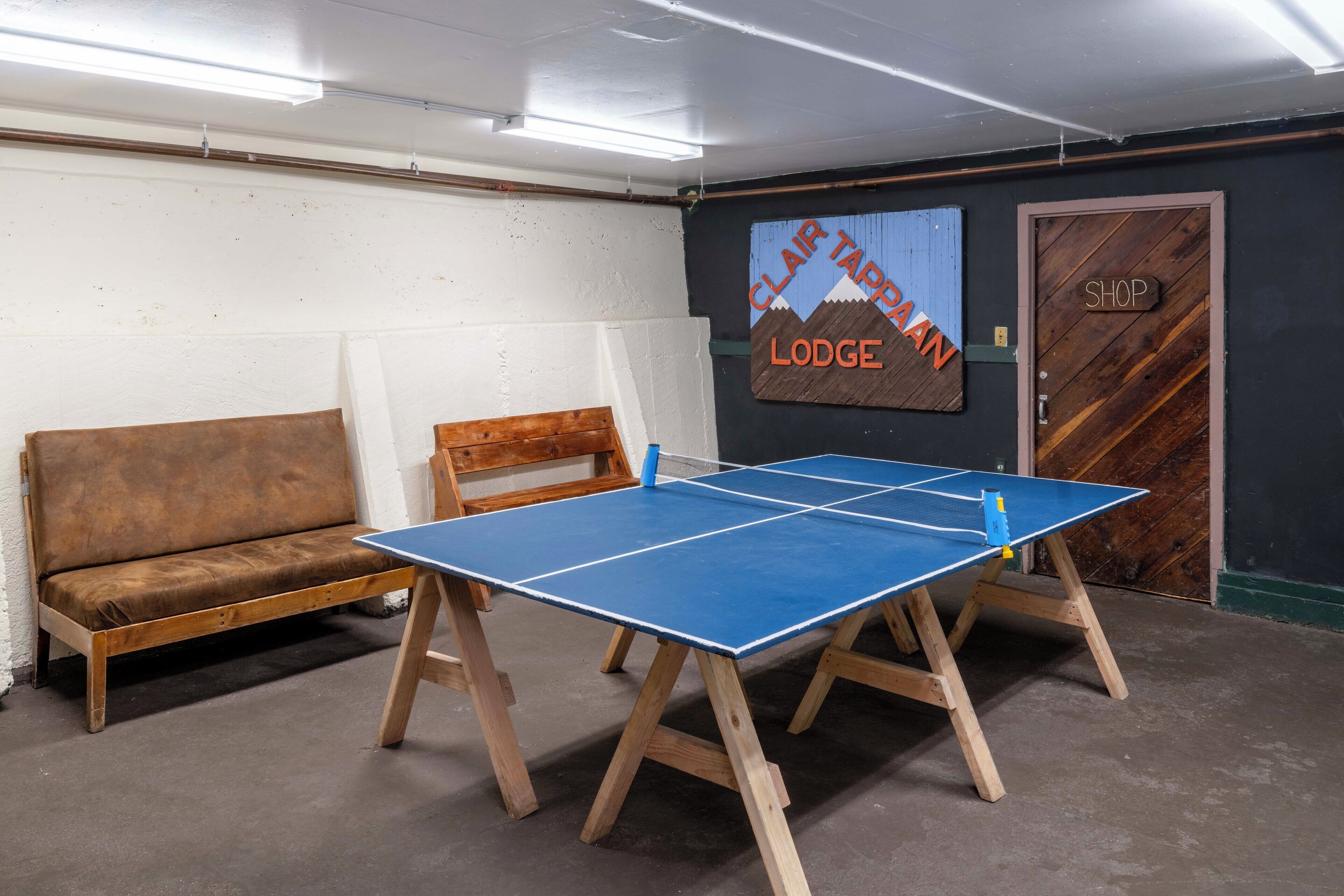 Taula de ping-pong en una habitació amb un sofà i una porta amb la inscripció "SHOP".