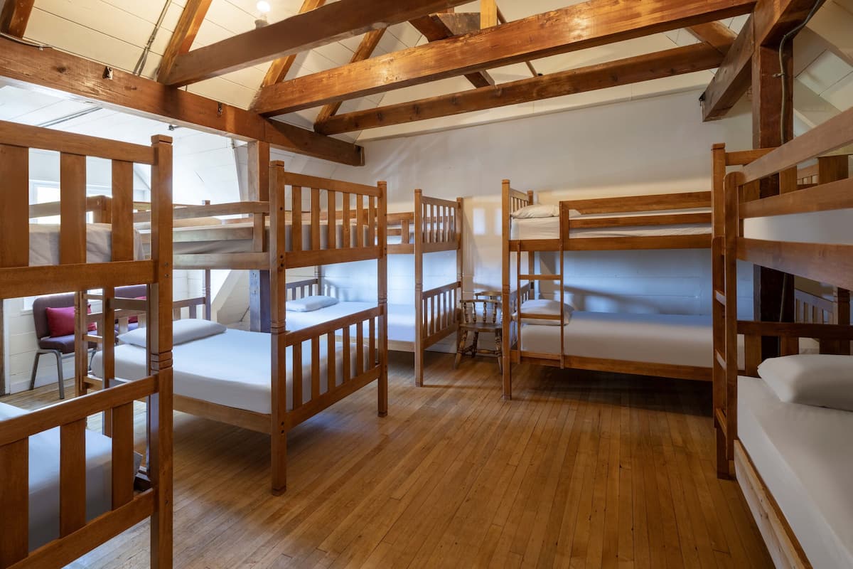 Un dormitorio con literas, piso de madera y una silla sencilla.