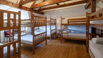 Un dormitorio con literas, piso de madera y una silla sencilla.