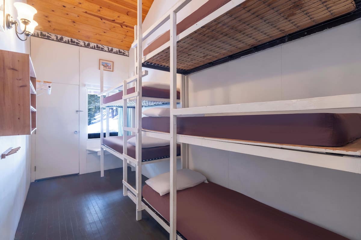 Dormitorio con literas, techo de madera, paredes blancas y ventana con vista a árboles.