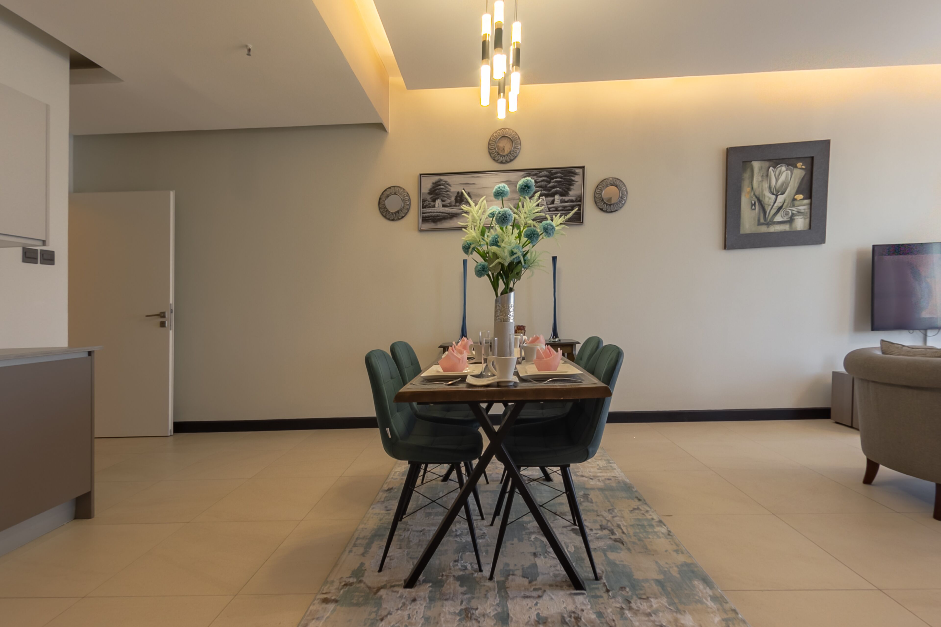 A dining area with a table set for four, a vase with flowers, and wall art.