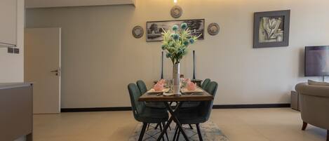 A dining area with a table set for four, a vase with flowers, and wall art.