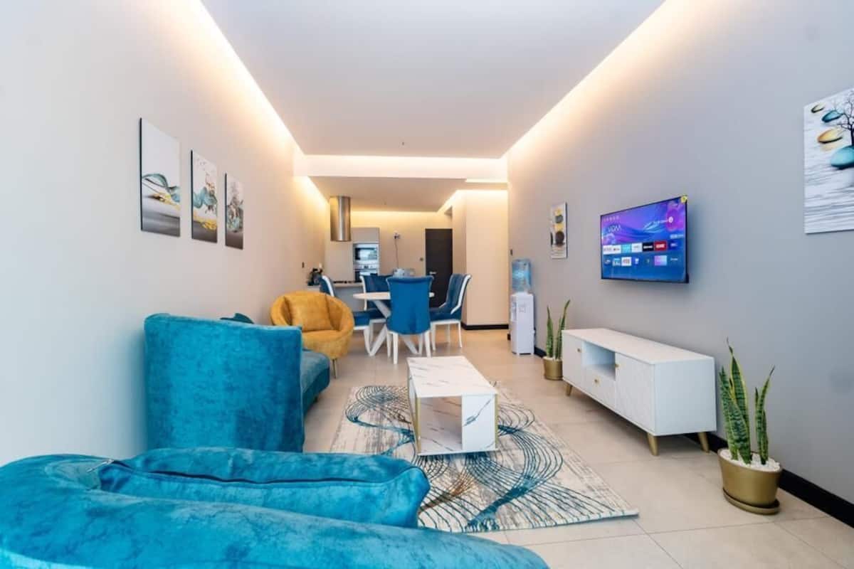 A modern living room with a blue sofa, a coffee table, and a TV on the wall.