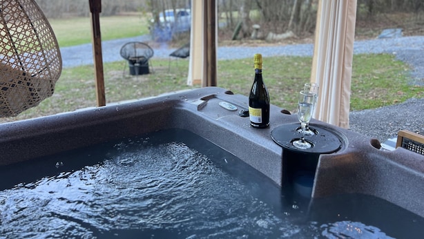 Una vasca idromassaggio con una bottiglia di champagne e un bicchiere, circondata da una poltrona in vimini e vista su un giardino.