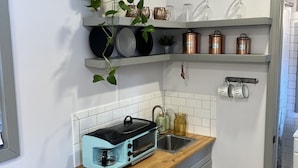 Una cucina compatta con un tostapane, mensole con pentole e una pianta in vaso.