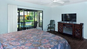 A bedroom with a large bed, a television, and a sliding glass door leading to a patio with a table and chairs.