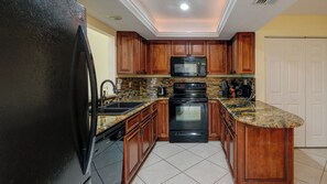 A kitchen with wooden cabinets, a black refrigerator, a microwave, a stove, and a sink.