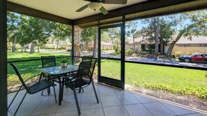 A covered patio with a table and chairs, large windows, and a view of a residential street.