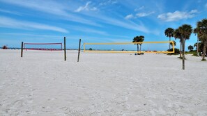 A beach volleyball court with two nets, one red and one yellow, and palm trees in the background.