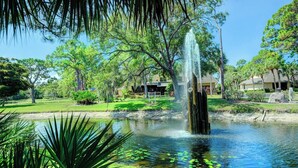 A tranquil pond with a central fountain, surrounded by lush greenery and trees.