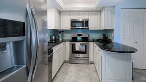 A modern kitchen with white cabinetry, a stainless steel refrigerator, a microwave, a stove, and a sink.