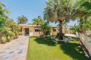 A residential property with a paved driveway, a well-maintained lawn, and a patio area with outdoor furniture. - 4BR W/Private Pool | Cozy Villa Near Beaches (Aruba)