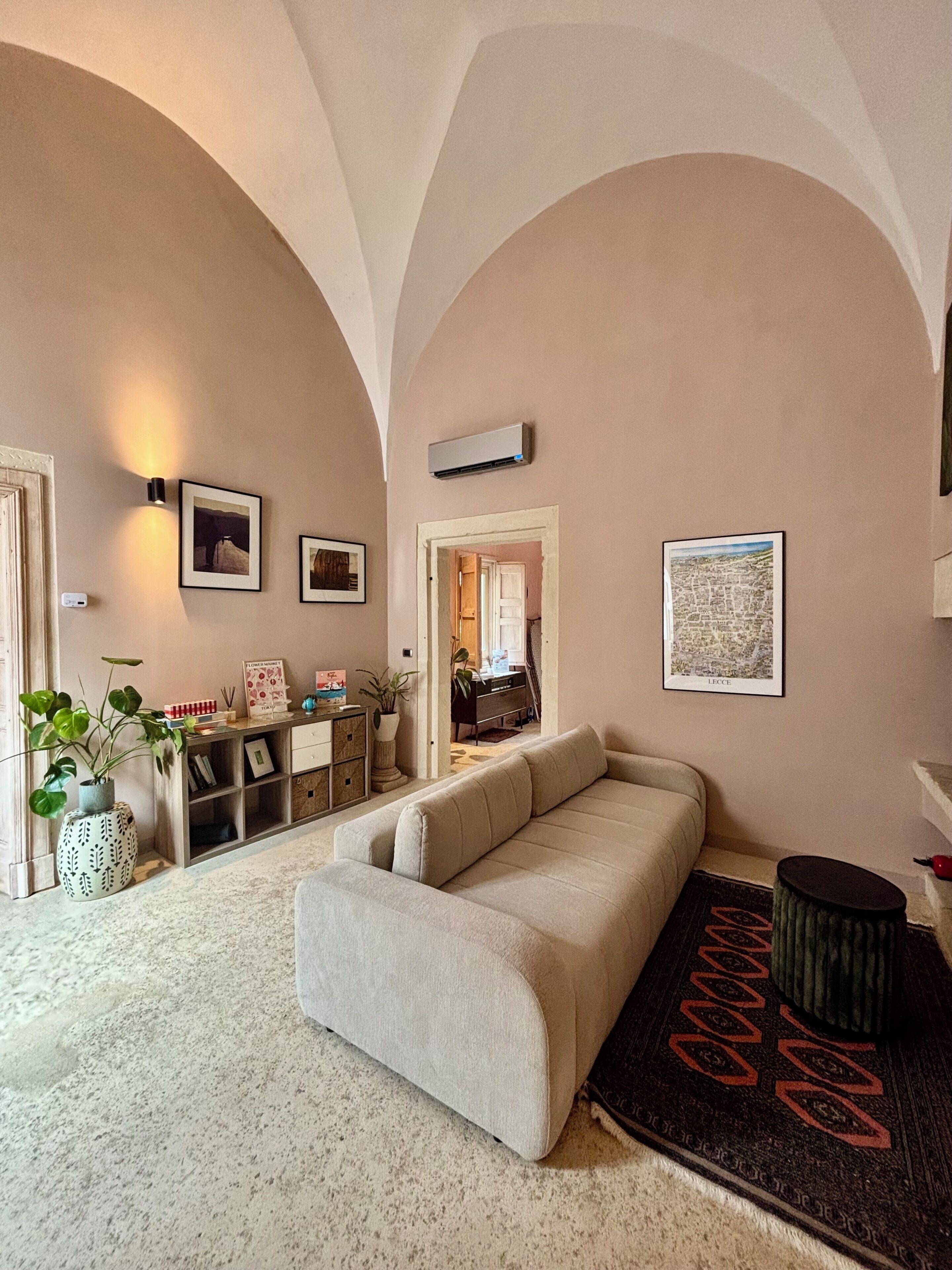 A living room with a sofa, a coffee table, a potted plant, and a wall-mounted air conditioner.