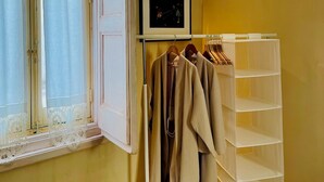 Una habitación con ventana, un perchero con ropa colgada, un cuadro en la pared y un mueble de almacenamiento blanco.