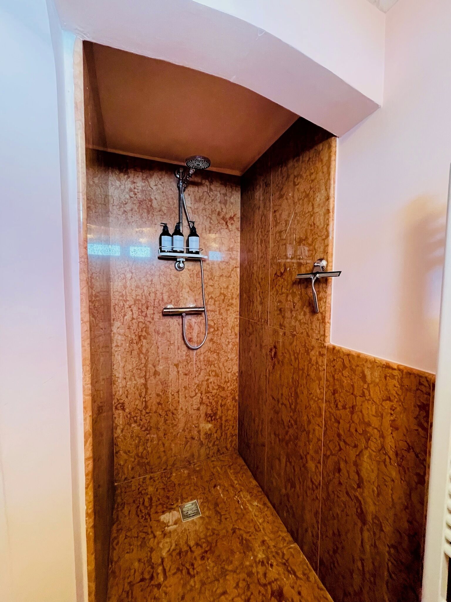 A small, enclosed shower area with a marble wall, a handheld showerhead, and a handheld shower attachment.