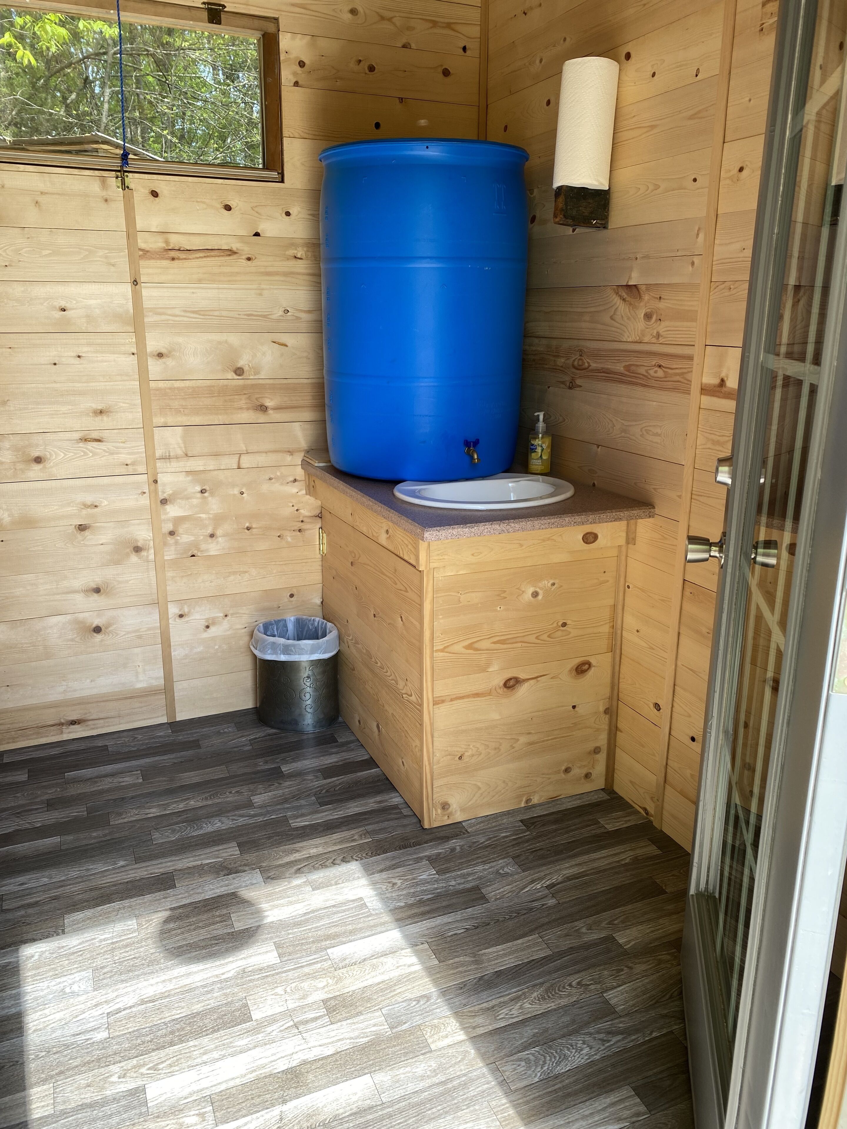 Une petite salle de bain en bois avec un tonneau bleu, un lavabo et une poubelle.