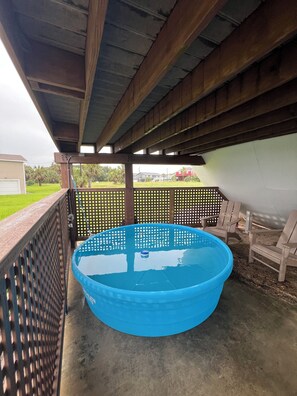 A covered outdoor swimming pool with a wooden deck and a fence.