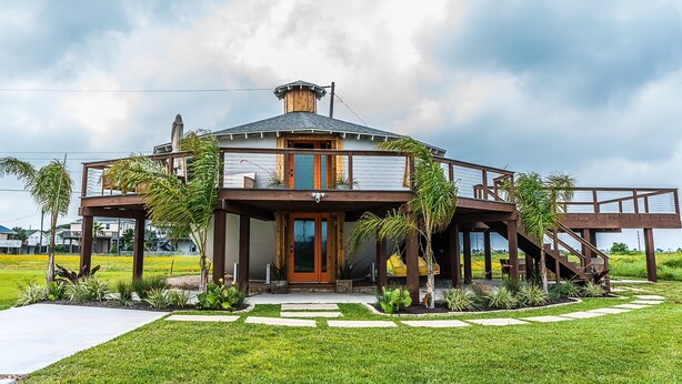 A modern house with a circular design, a wooden deck, and a staircase leading to an upper level.