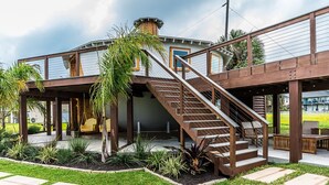 A modern house with a covered patio, a wooden staircase, and a well-maintained garden.