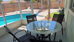 Un patio cubierto con una mesa y sillas de vidrio, una piscina y una valla de madera al fondo.