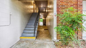 A narrow stairwell with a metal railing, a 'No Dogs Allowed' sign, and a brick wall on one side.