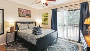 A bedroom with a bed, a ceiling fan, a window with curtains, and artwork on the walls.