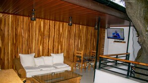 Un interior de madera con un sofá, sillas, una mesa con cubierta de vidrio y un televisor montado en la pared.
