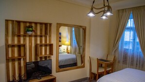 Una habitación de hotel con una cama, un escritorio, un televisor y un espejo.