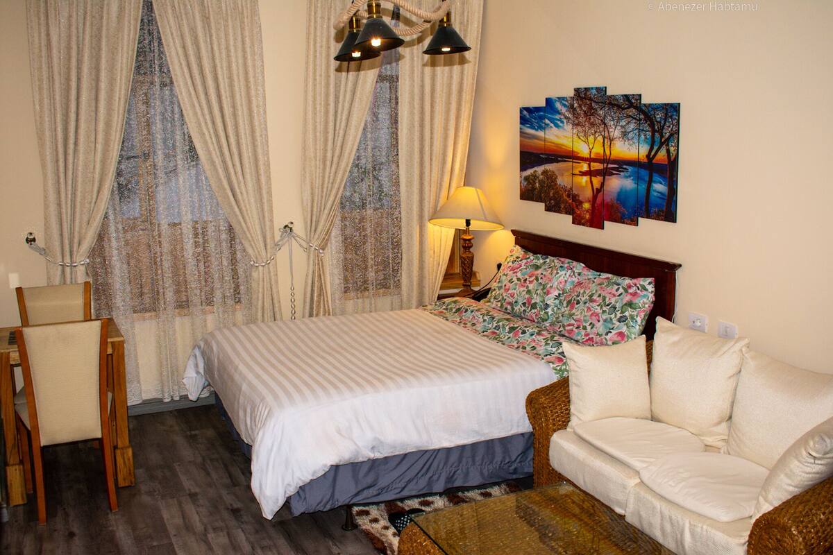 A bedroom with a bed, a sofa, a chair, a lamp, and a painting on the wall.
