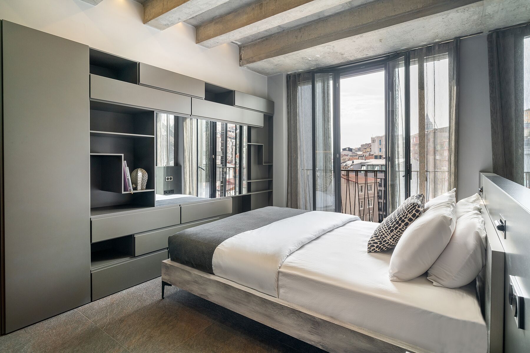 Camera da letto moderna con mobili a incasso, un'ampia finestra vista città e un letto con biancheria da letto bianca.