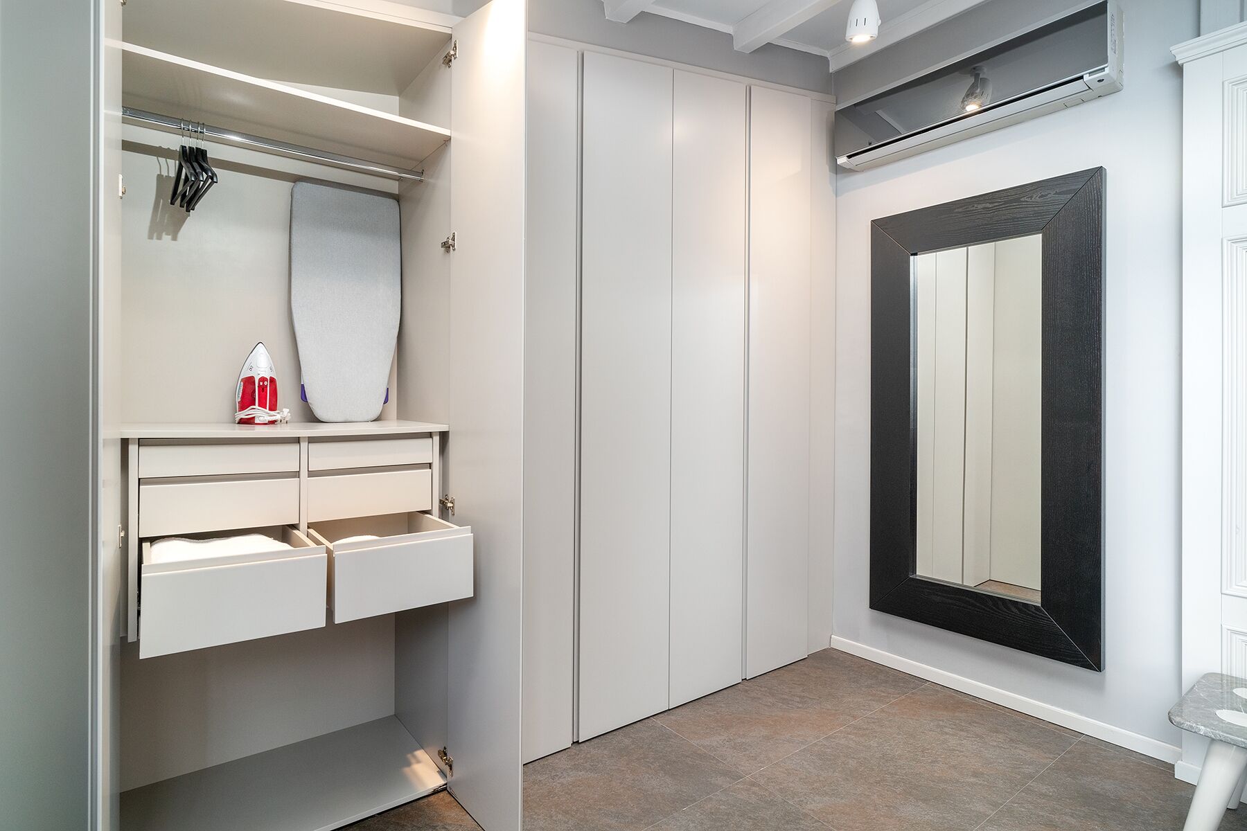 A walk-in closet with a mirrored wardrobe, a hanging rack, and a small ironing board.