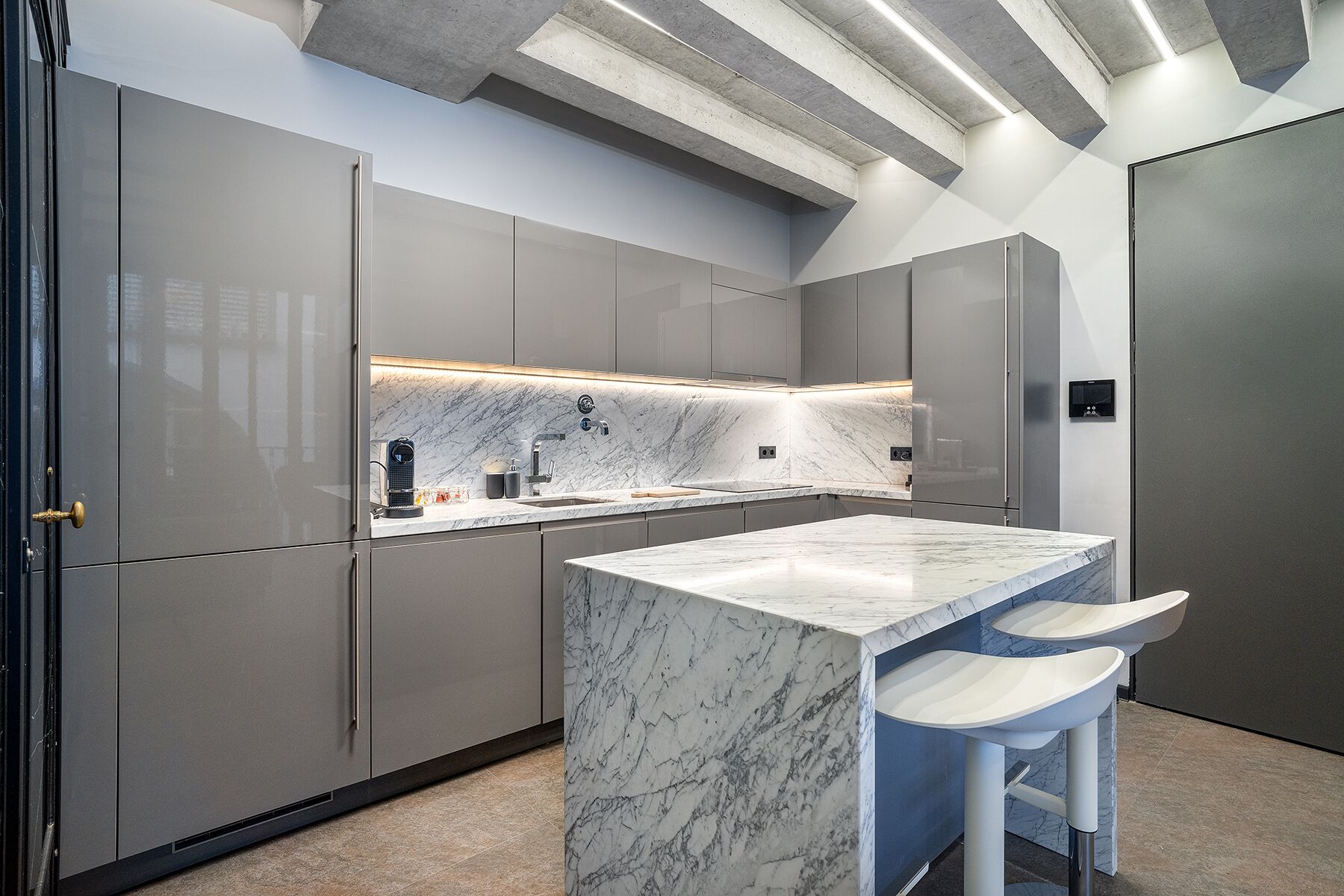 A modern kitchen with grey cabinetry, a marble countertop, and a built-in island with bar stools.