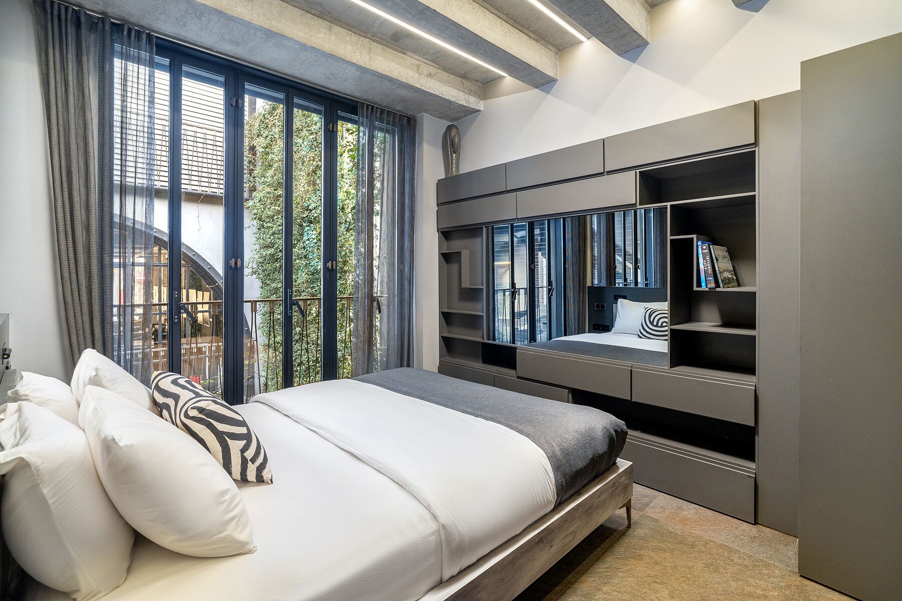 A modern bedroom with a large bed, built-in shelving, and a view of the outdoors.