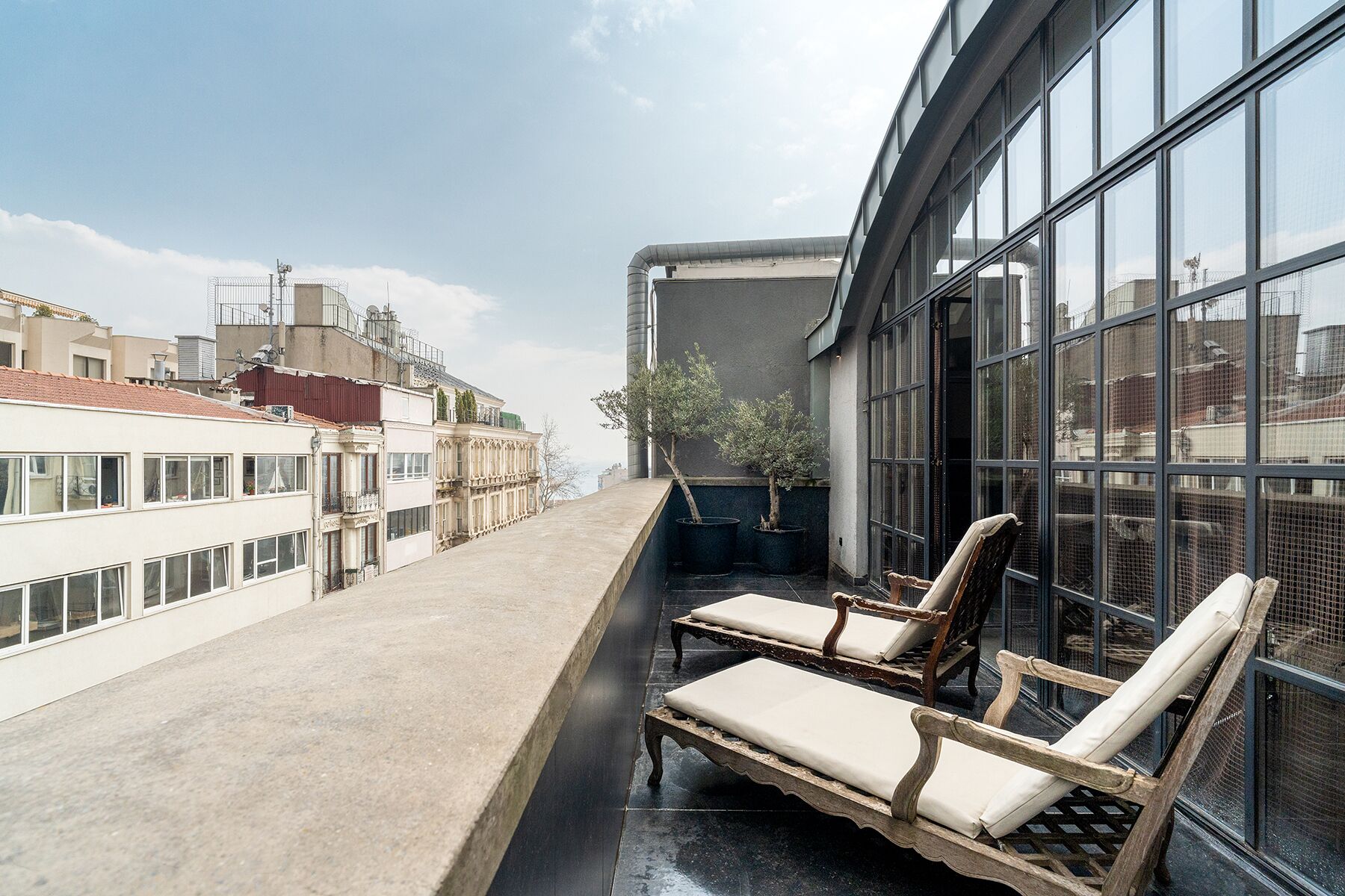 A rooftop terrace with two wooden lounge chairs and a small potted tree.