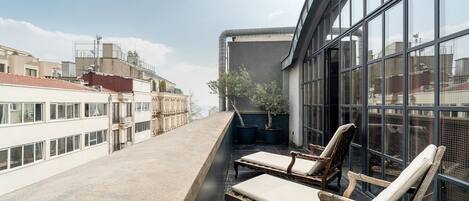 A rooftop terrace with two wooden lounge chairs and a small potted tree.