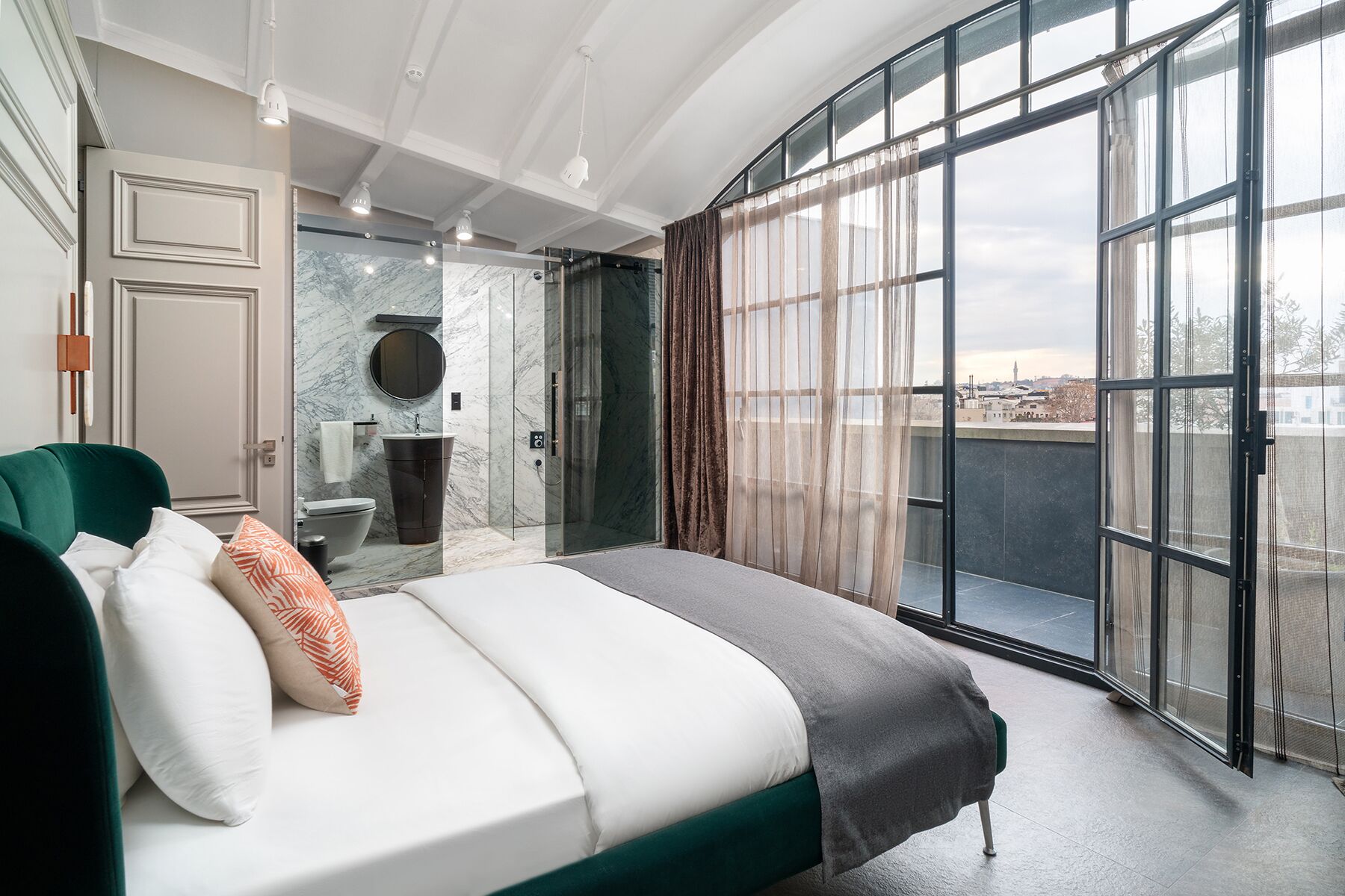Una camera da letto moderna con un letto, un bagno e un balcone con ampie finestre.