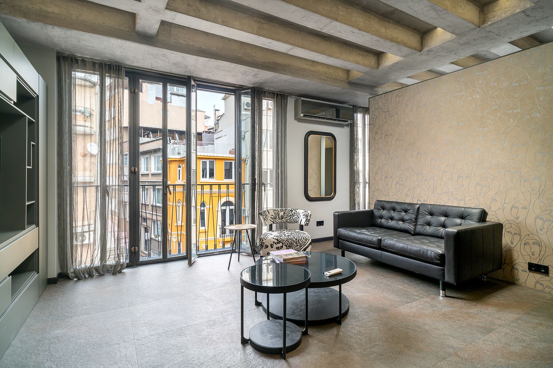 Una sala moderna con un sofá de cuero negro, una mesa de centro de vidrio y un ventanal con vistas a edificios.
