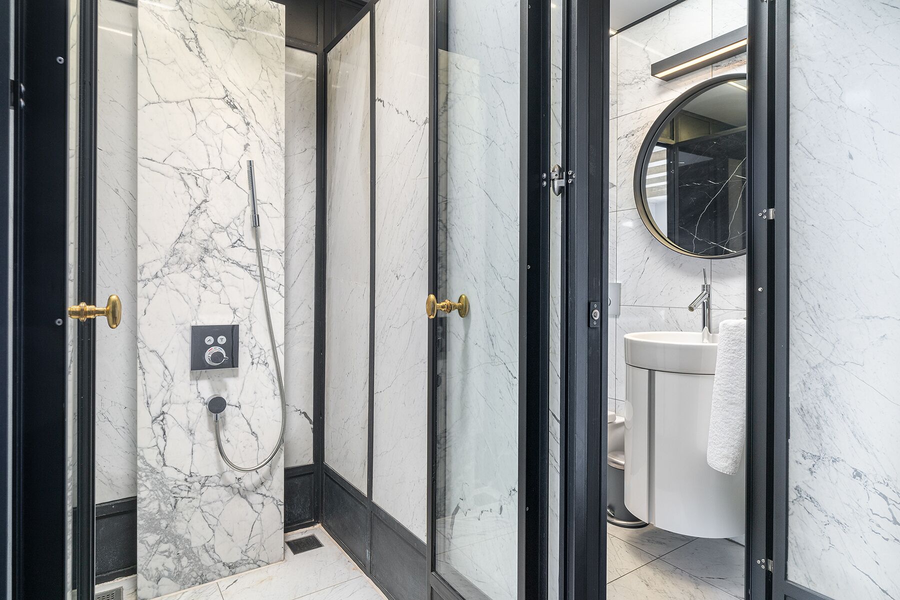 A modern bathroom with a marble shower, a round mirror, and a white sink.