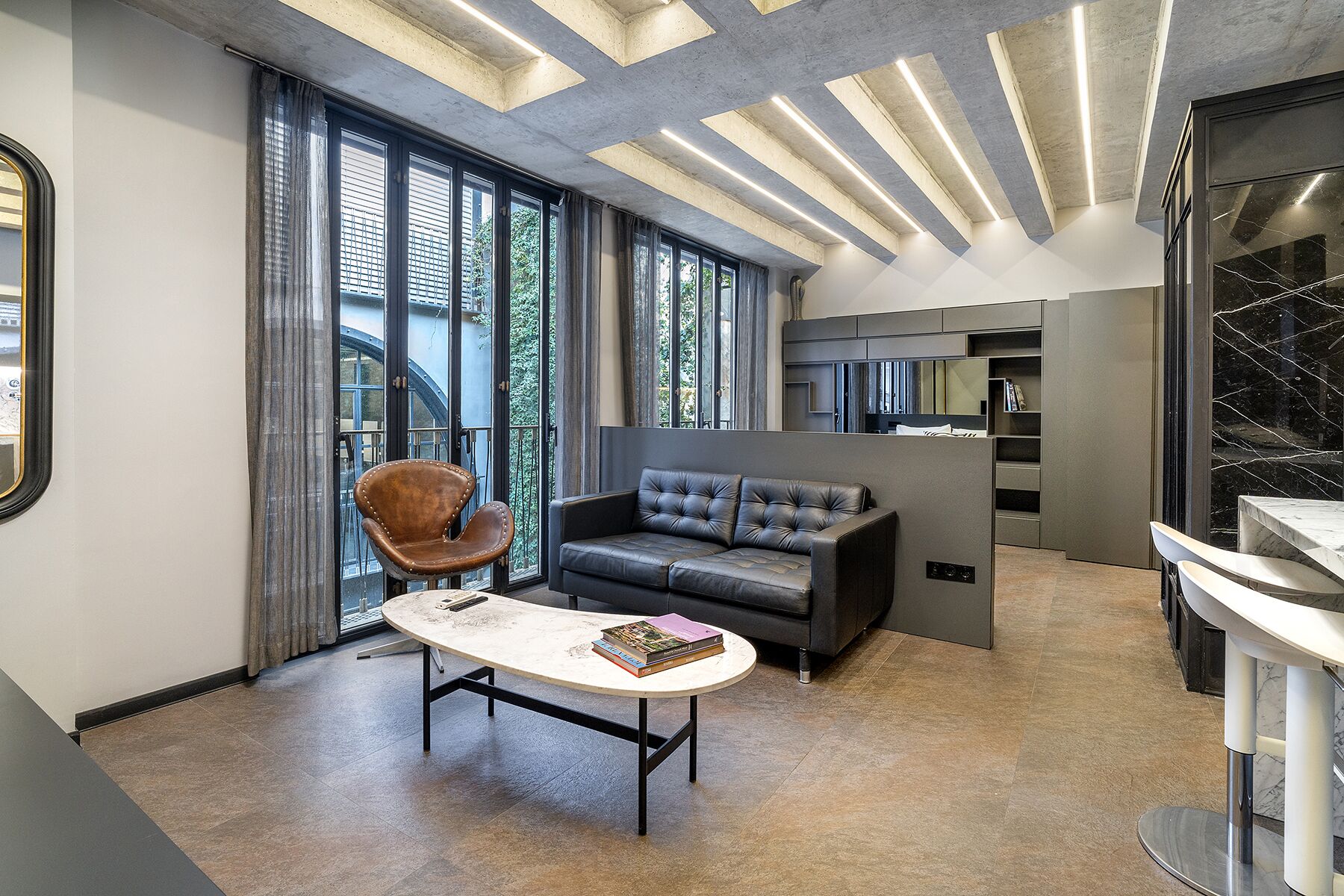 Un salon moderne avec un canapé en cuir, une table basse ronde et une grande fenêtre agrémentée de rideaux.