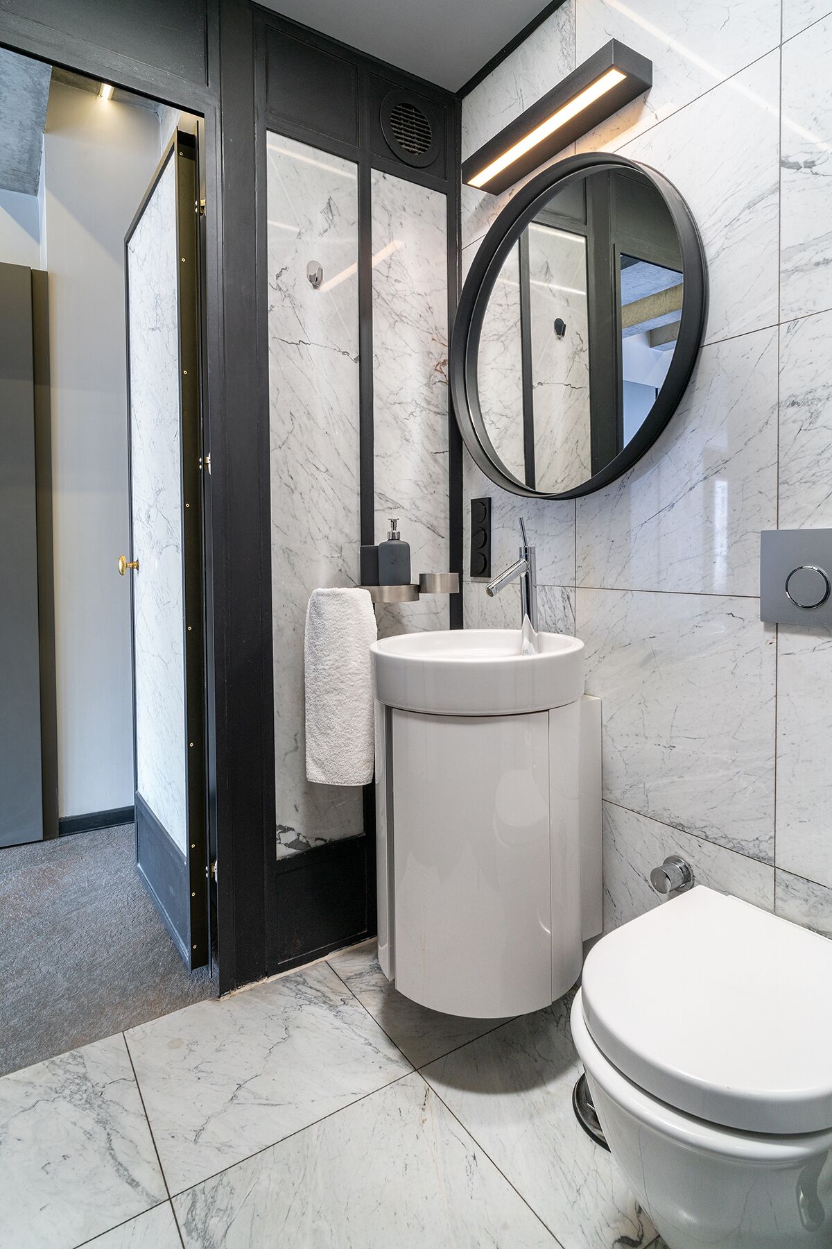 Et moderne badeværelse med en hvid vask, et rundt spejl og et toilet.
