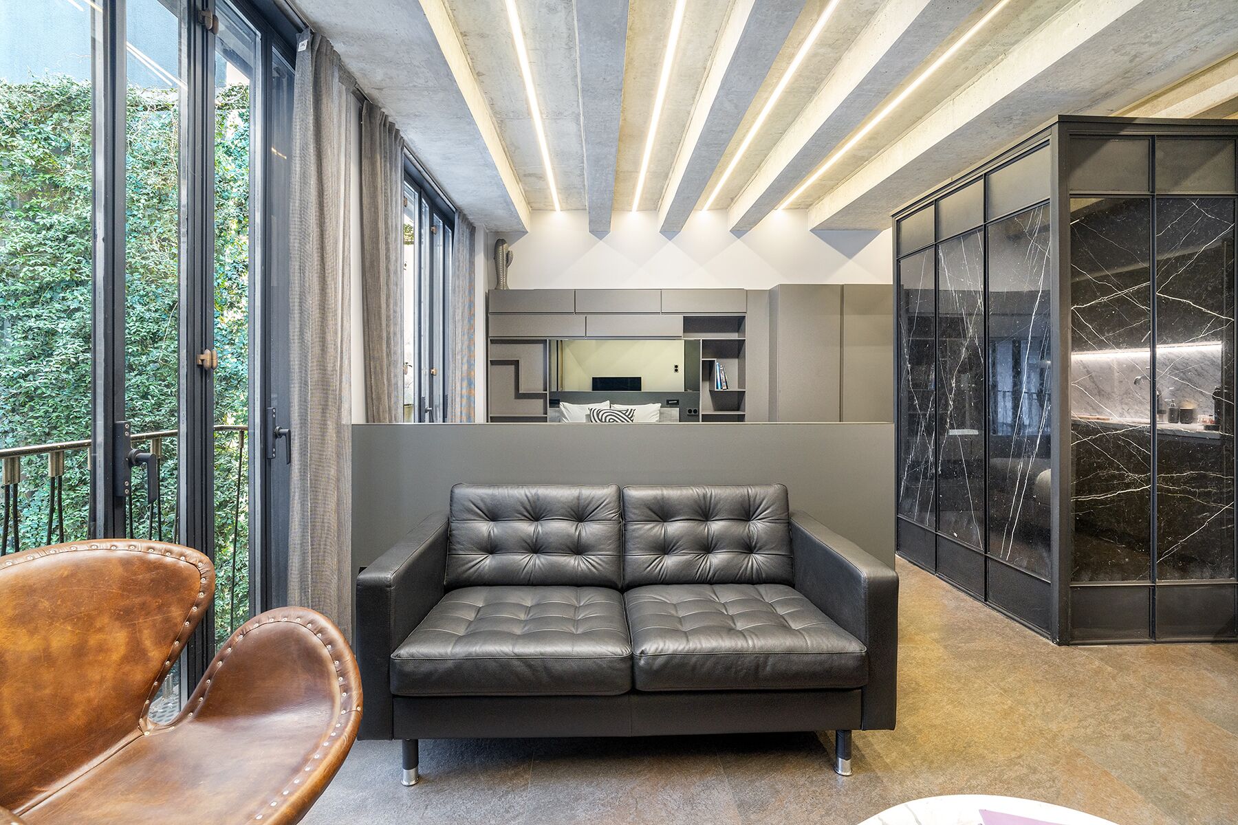 Una sala de estar moderna con un sofá de cuero, un sillón de cuero marrón y un ventanal con vistas a zonas verdes.
