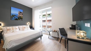 A modern hotel room with a bed, a desk, a chair, a TV, and a balcony with a view of buildings. - Ponte di Tappia Suites (Naples)