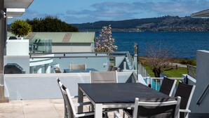 A balcony with a table and chairs, overlooking a lake and a distant town. - Waimahana 5 - Taupo Holiday Apartment (Taupo)