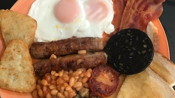 Un plato con huevos, tocino, salchichas, frijoles, champiñones, tostadas y una rebanada de morcilla.